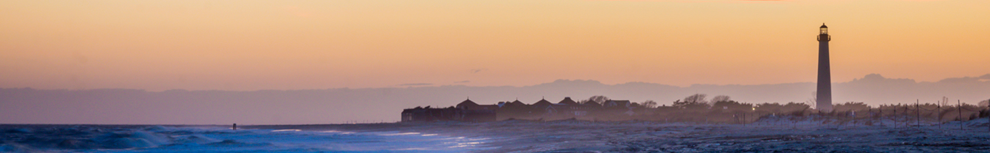 Cape May Lighthouse in New Jersey from the water, with a hazy orange skyline at dusk